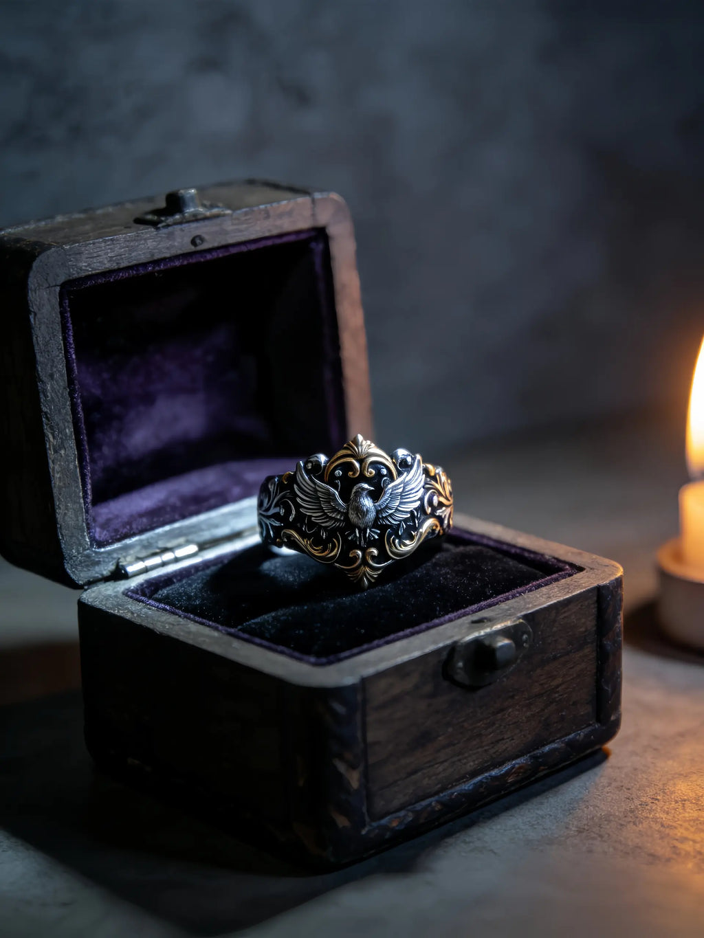 Baroque Raven Crest Ring displayed in a wooden ring box beside candlelight