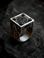 Heavy Gothic cathedral signet ring on textured black stone, showing the rose window face and chunky band