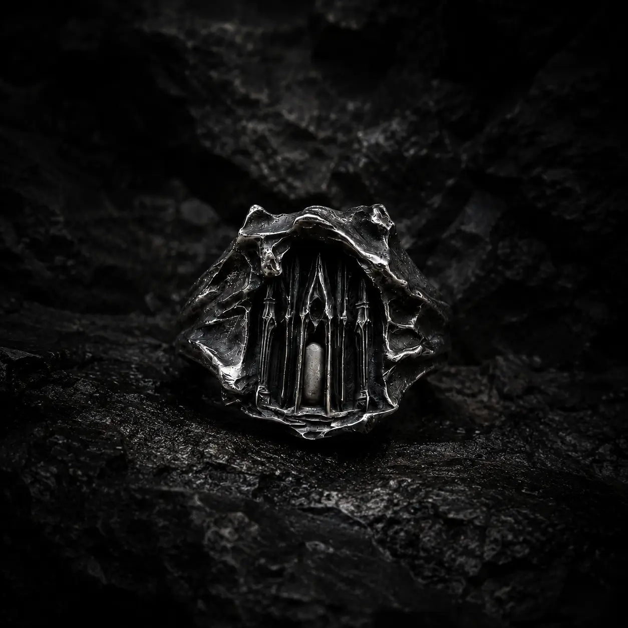 Dark Cathedral Ring — a miniature Gothic cathedral façade carved into raw oxidized 925 sterling silver, front view on dark rock