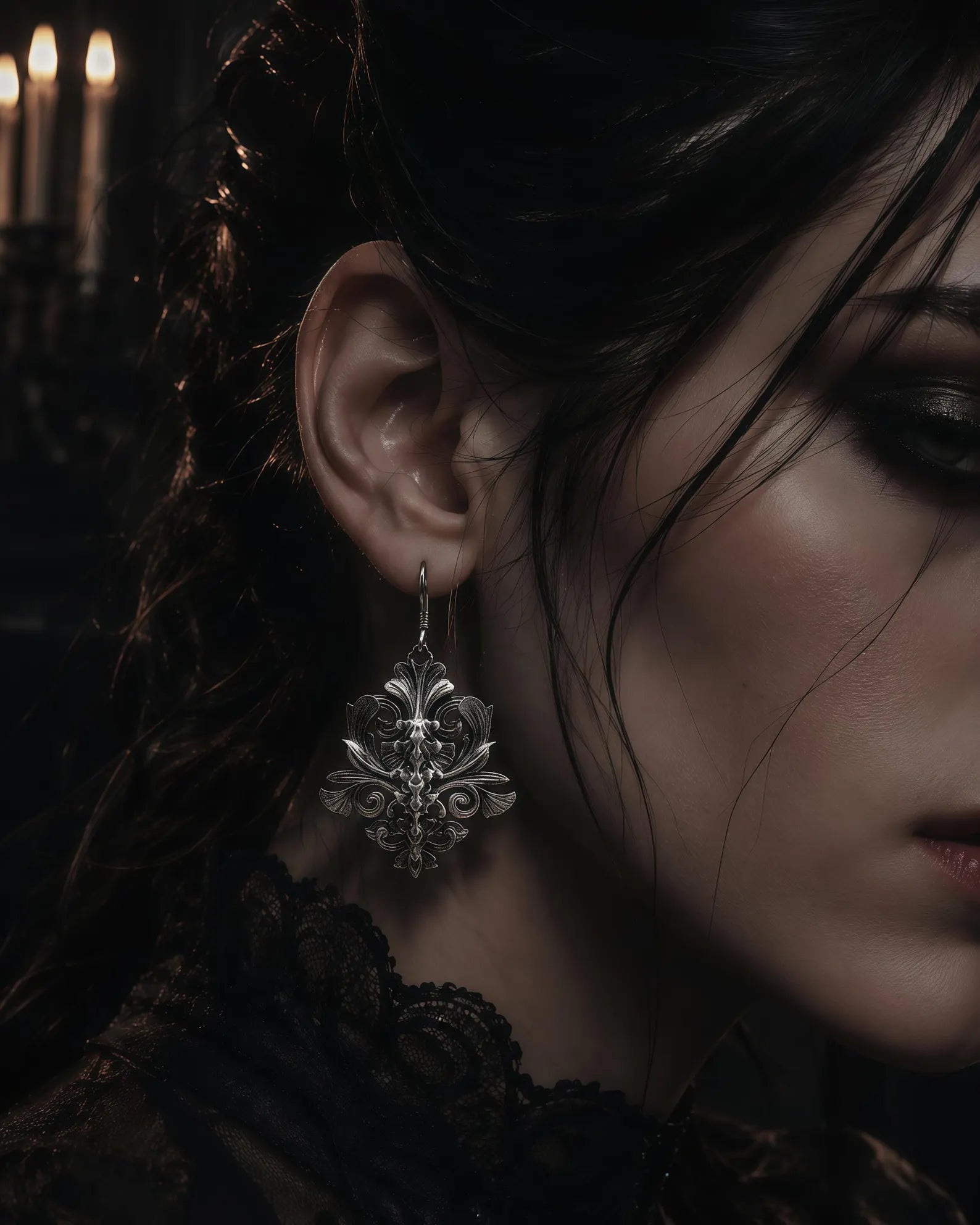 Iris motif gothic dangle earring worn in ear, close-up with candlelight background