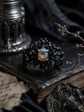 Dark Bloom Ring — black oxidized 925 sterling silver bloom of thorns and coral around an iridescent oval opal, on a dark book